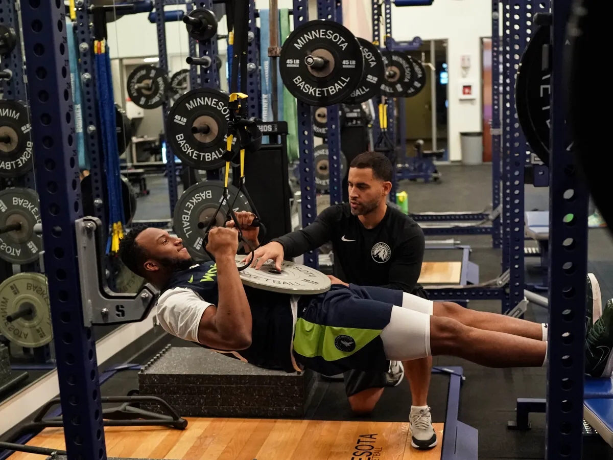 Bill Burgos coaching a Minnesota Timberwolves player through a suspended-strap row in the team weight room