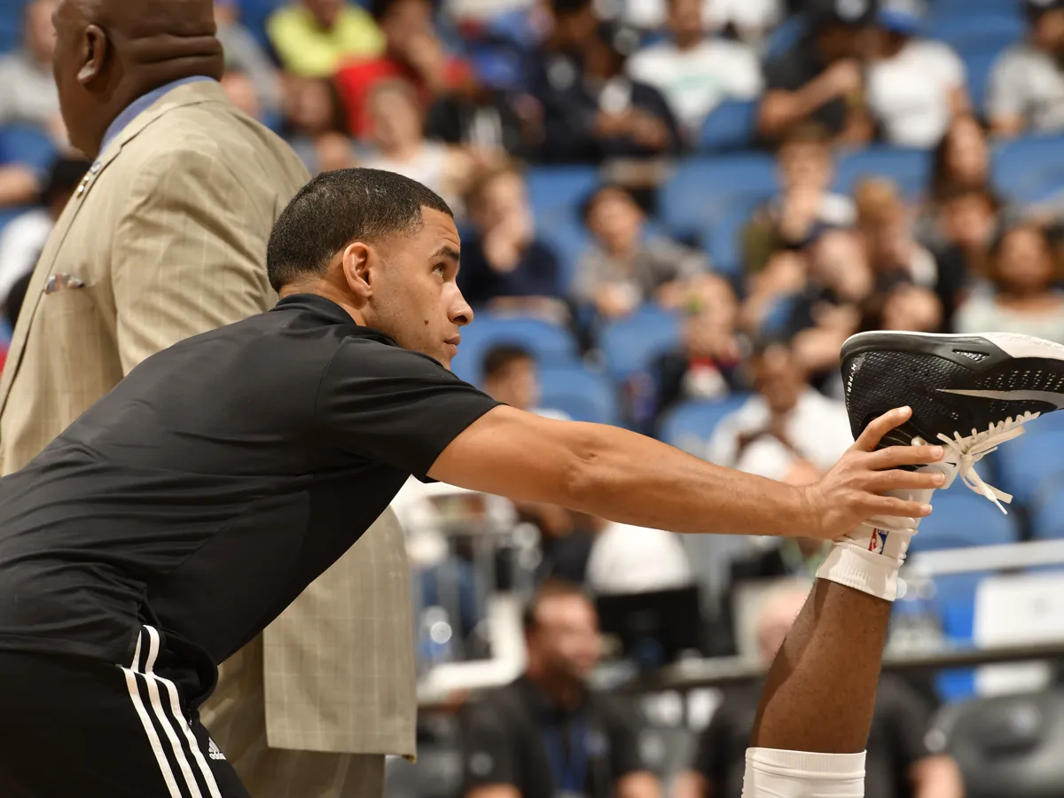 Bill Burgos stretching an Orlando Magic player's leg courtside before a game